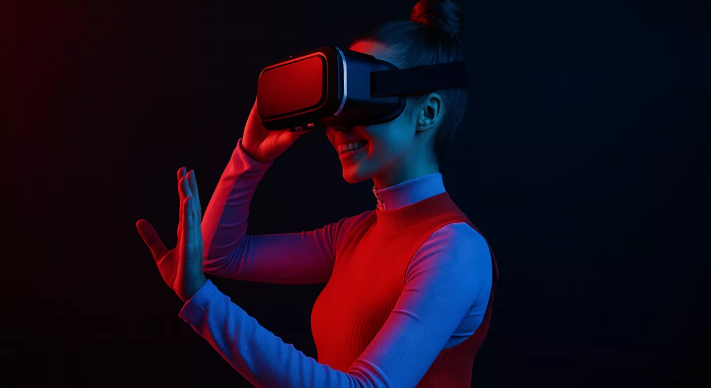 A person wearing a VR headset in a dark room lit with red and blue lights, smiling and reaching forward as if interacting with virtual objects.