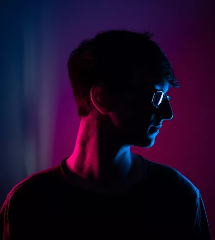 Silhouetted person wearing glasses in moody blue and pink neon lighting, head turned to the side, with color gradients highlighting face and neck.